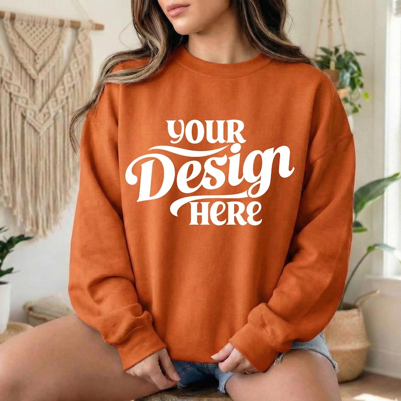 May include: An orange sweatshirt with the text "YOUR Design HERE" in white script. The long-sleeved top is a solid color and appears to be made of a soft material. The sweatshirt is a casual style.