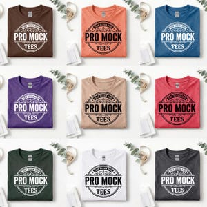 May include: Nine folded t-shirts in various colors, including brown, peach, blue, purple, tan, red, green, white, and gray. Each shirt features the text "PRO MOCK TEES" in a circular design. The shirts are arranged on a white surface.