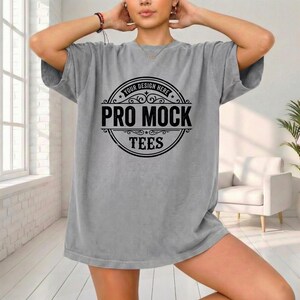 May include: A gray t-shirt with a large circular graphic in black. The graphic reads "YOUR DESIGN HERE" at the top, with "PRO MOCK TEES" in a bold font below. The shirt is oversized and has short sleeves.