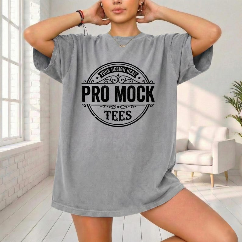 May include: A gray t-shirt with a large circular graphic in black. The graphic reads "YOUR DESIGN HERE" at the top, with "PRO MOCK TEES" in a bold font below. The shirt is oversized and has short sleeves.