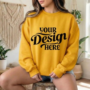 May include: Mustard yellow sweatshirt with the text "YOUR Design HERE" in black script. The long-sleeved crew neck top is a solid color and is suitable for casual wear. The sweatshirt is made of a soft material.