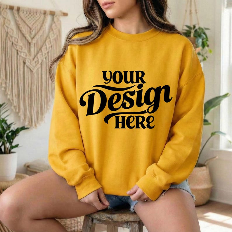 May include: Mustard yellow sweatshirt with the text "YOUR Design HERE" in black script. The long-sleeved crew neck top is a solid color and is suitable for casual wear. The sweatshirt is made of a soft material.