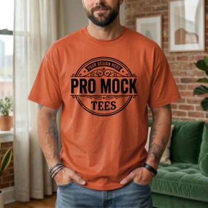 May include: Orange t-shirt with a black circular graphic that reads "PRO MOCK TEES" with "YOUR DESIGN HERE" at the top. The shirt is a solid orange color and has short sleeves. The person is wearing a black bracelet.