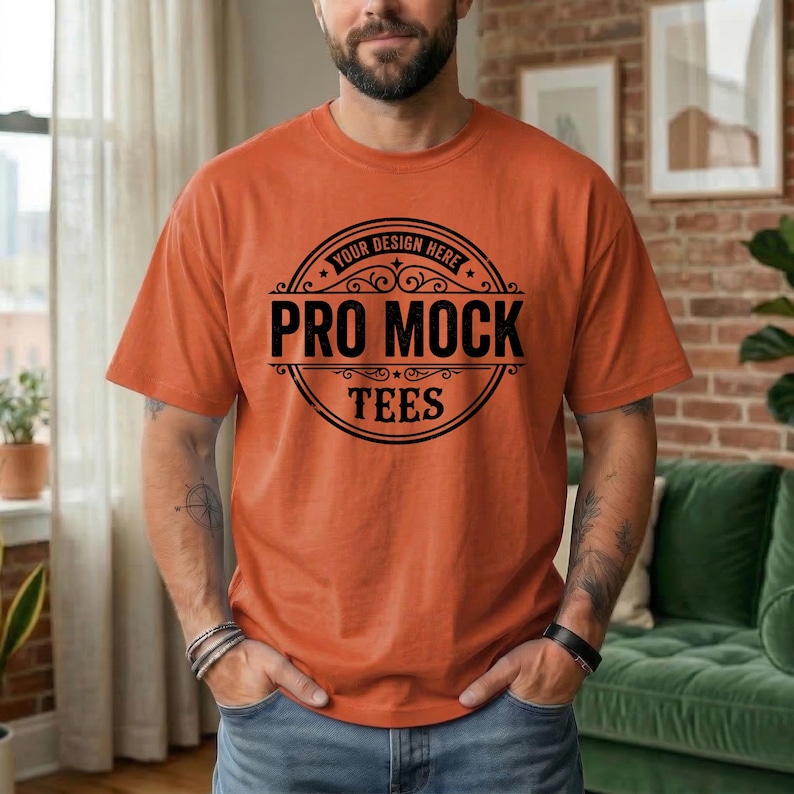 May include: Orange t-shirt with a black circular graphic that reads "PRO MOCK TEES" with "YOUR DESIGN HERE" at the top. The shirt is a solid orange color and has short sleeves. The person is wearing a black bracelet.