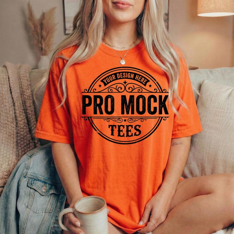 Peut inclure: Un t-shirt orange avec le texte "PRO MOCK TEES" dans un motif circulaire noir. Le t-shirt a des manches courtes et une coupe ample. Les mots "YOUR DESIGN HERE" sont au-dessus du texte principal.