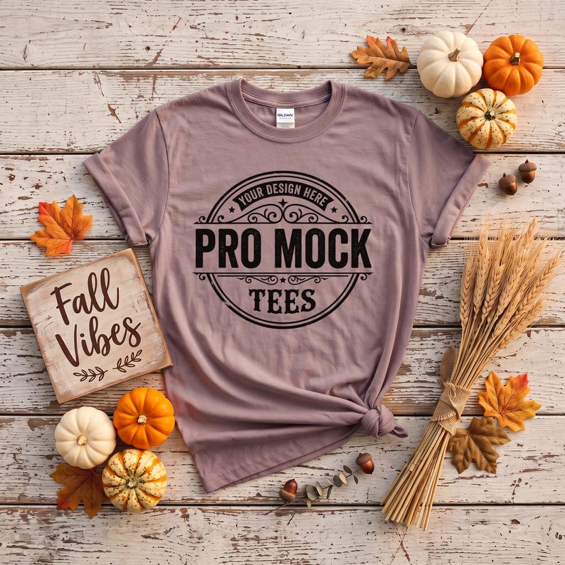 May include: A mauve short-sleeve t-shirt featuring a black circular graphic with the text "YOUR DESIGN HERE PRO MOCK TEES" in the center. The shirt has a crew neckline and is displayed flat with a square sign reading "Fall Vibes" nearby.