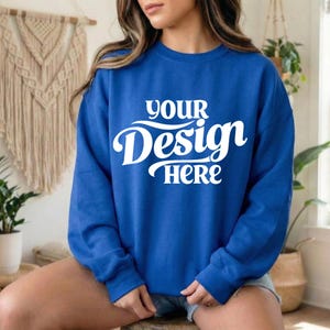 May include: A royal blue sweatshirt with the text "YOUR Design HERE" in white script. The long-sleeved crew neck top is made of a soft material. The sweatshirt is a versatile piece of apparel.