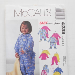May include: A sewing pattern for a child's pajamas. The pattern includes five different styles: a blue and white pajama with a moon and star print, a pink pajama with a ruffle trim, a yellow pajama with a dinosaur print, a pink shirt and pants set, and a pink and white striped shirt and pants set. The pattern is for sizes 1-2-3-4.