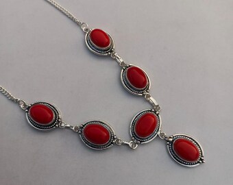 May include: A silver necklace featuring six oval, bright red gemstones. Each gemstone is set in a silver bezel and connected by silver links. The necklace has a delicate chain.