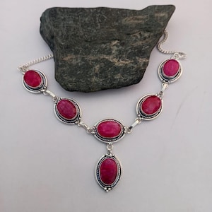 Könnte beinhalten: Eine silberne Halskette mit ovalen, tiefrosa Edelsteinen. Die Edelsteine sind in einem silbernen Rahmen mit einem Perlenrand gefasst. Die Halskette hat eine Kette und einen Anhänger mit ähnlichem Design.