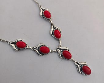 May include: A silver-toned necklace featuring oval, bright red gemstones. The necklace has a Y-shaped design with five gemstones. The gemstones are set in decorative, stylized silver settings. The chain is delicate.