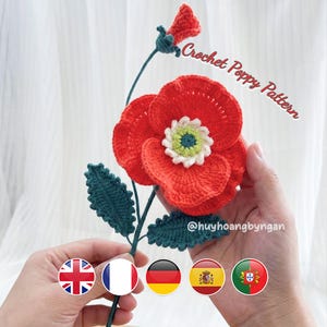 May include: A handmade crochet poppy flower in vibrant red, with a white and green center. The flower has green leaves and stem. The text "Crochet Poppy Pattern" is visible. The flower is held by hands.