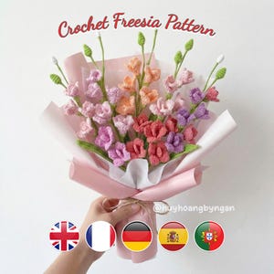 Könnte beinhalten: Ein Strauß gehäkelter Freesien in Rosa-, Pfirsich- und Lilatönen, verpackt in rosa Papier. Der Text "Crochet Freesia Pattern" ist zu sehen. Der Strauß wird von einer Hand gehalten.