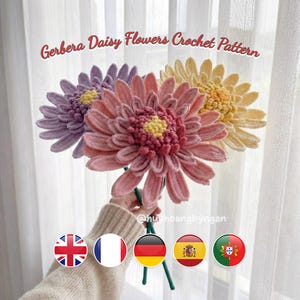Op de afbeelding: Een boeket gehaakte gerbera madeliefjes in paars, roze en geel. De bloemen hebben gele centra en groene stelen. De tekst "Gerbera Daisy Flowers Crochet Pattern" staat bovenaan de afbeelding.