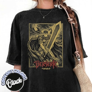 Puede incluir: Camiseta negra Comfort Colors con un gráfico dorado y rojo de un guerrero sosteniendo una gran espada, con la palabra "BERSERK" en rojo y texto japonés. La camiseta tiene un aspecto vintage y desgastado.