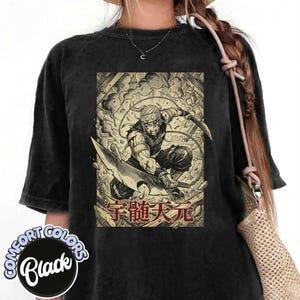 Peut inclure: T-shirt noir Comfort Colors avec une illustration détaillée d'un guerrier maniant une grande lame, sur fond de scène de bataille. Le motif comprend du texte japonais en rouge. Le t-shirt a un aspect vintage.