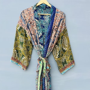 May include: A colorful paisley-patterned robe with long sleeves, hanging on a wooden hanger. The robe features a mix of blue, green, pink, and gold hues. A matching fabric belt is tied at the waist. The robe is made of a lightweight material.