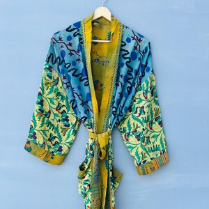 Può includere: Una vestaglia a maniche lunghe con un design patchwork caratterizzato da vari motivi floreali e geometrici nei toni del blu, giallo e verde. Il capo include una cintura in vita coordinata e un bordo giallo a contrasto sul davanti.