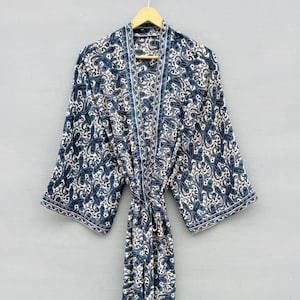 May include: A long-sleeved robe featuring a dark blue and white paisley pattern throughout. The garment includes a matching fabric tie belt at the waist, wide sleeves, and a straight front opening with a decorative border trim along the edges.
