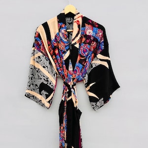 May include: A long-sleeved kimono robe featuring a vibrant patchwork design. The garment displays a mix of black, cream, blue, and red colors with intricate paisley and floral patterns throughout. It includes a matching fabric tie belt at the waist.