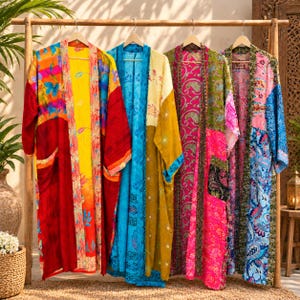 May include: Four long, open-front robes hanging on a wooden rack. The first is red and yellow with floral patterns. The second is blue and mustard yellow with geometric prints. The third is pink and green with paisley designs. The fourth is blue and pink with floral motifs.