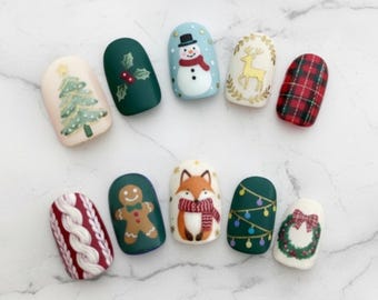 May include: A collection of ten Christmas-themed nail art designs. Each nail features a unique design, including a Christmas tree, snowman, reindeer, plaid pattern, and a gingerbread man. The nails are painted in various colors, including green, red, and white.
