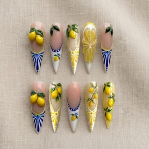 May include: A collection of ten long, pointed artificial nails with a lemon theme. Each nail features a different design, including 3D lemons, painted lemons with leaves, and intricate yellow and white patterns. The nails have a glossy finish.