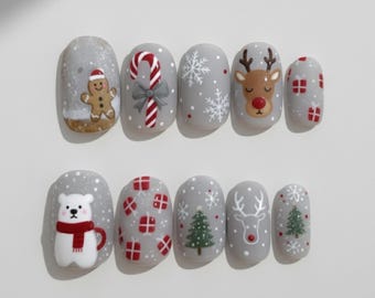 May include: A set of gray press-on nails with Christmas-themed designs. Each nail features a different festive design, including a gingerbread man, candy cane, snowflakes, reindeer, gift boxes, a polar bear with a mug, and Christmas trees.