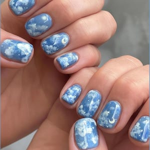 May include: Short, rounded fingernails featuring a glossy sky-blue base coat with hand-painted white clouds, tiny sparkling stars, and small crescent moon accents. The design covers the entire nail surface, creating a cohesive night sky theme.