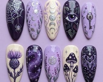 Op de afbeelding: Een set van tien amandelvormige kunstnagels met gedetailleerde handgeschilderde ontwerpen in tinten paars, crème en zilver. De motieven omvatten een spinnenweb, hemellichamen, maanfasen, een oog, een hartvormige sleutel, een distel, sterren, een pentagram, paddenstoelen en een vleermuis.