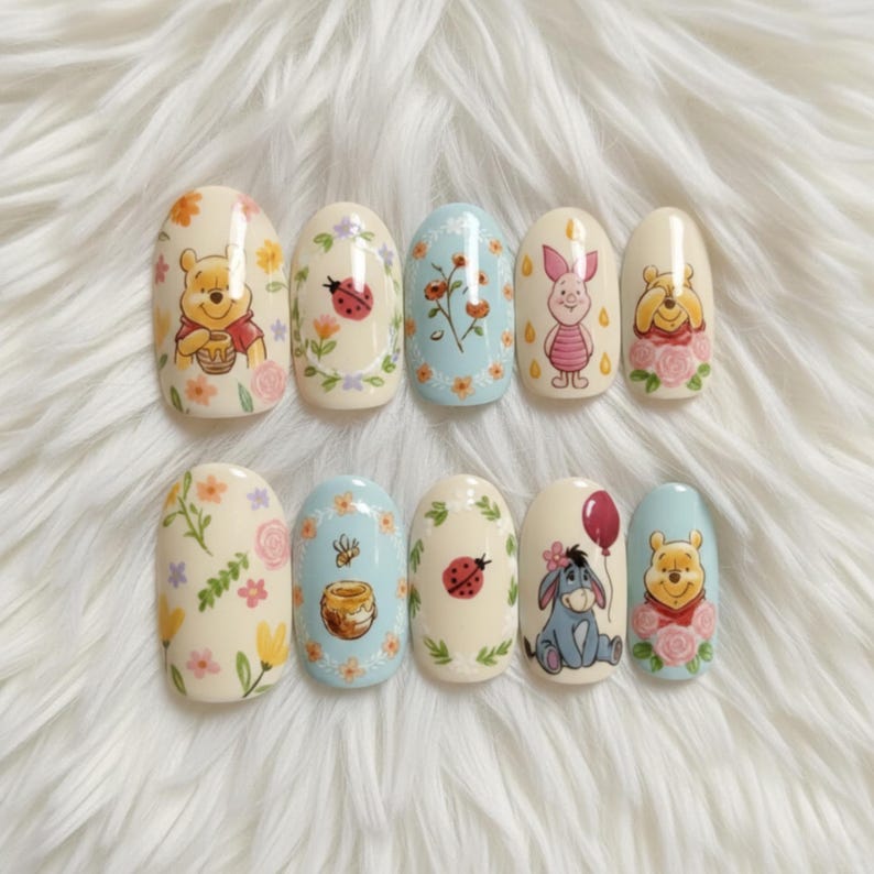May include: Set of ten artificial nails with Winnie the Pooh and friends designs. Each nail features a different character or element from the series, including Pooh Bear, Piglet, Eeyore, honey pots, and floral accents. The nails are oval-shaped and painted in pastel colors.