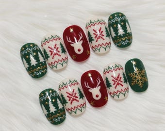 May include: A set of ten artificial nails with a festive Christmas theme. The nails feature designs including a reindeer, snowflakes, and Christmas trees in red, green, white, and gold. The nails are oval-shaped.