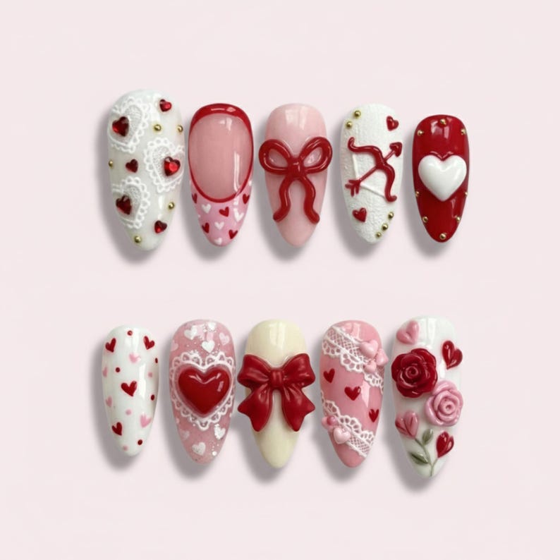 May include: A set of ten almond-shaped press-on nails featuring various designs in red, white, and pink. Decorations include 3D red bows, white lace patterns, red and white hearts, a cupid bow and arrow, and sculpted red and pink roses.
