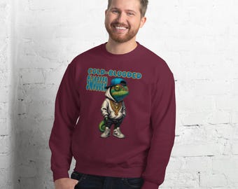May include: Burgundy sweatshirt featuring a cartoon chameleon wearing a blue cap, gold chain, and white hoodie. The text "COLD-BLOODED SWAGGER" is above the chameleon. The sweatshirt is a solid color.