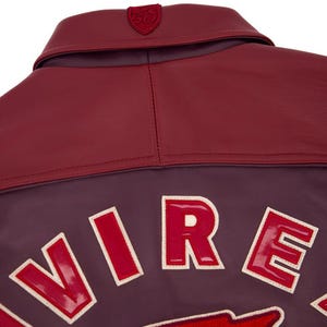 Może przedstawiać: Zbliżenie na tył bordowej sk&oacute;rzanej kurtki. Kurtka posiada bordowy kołnierz i ciemnofioletowy korpus z białymi, czerwonymi literami, kt&oacute;re piszą "VIRE". Mały emblemat znajduje się na kołnierzu.