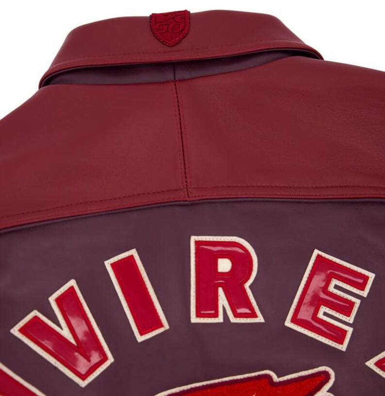 Może przedstawiać: Zbliżenie na tył bordowej sk&oacute;rzanej kurtki. Kurtka posiada bordowy kołnierz i ciemnofioletowy korpus z białymi, czerwonymi literami, kt&oacute;re piszą "VIRE". Mały emblemat znajduje się na kołnierzu.