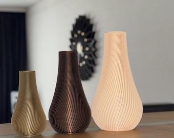 May include: Three decorative vases in varying sizes and colors. The smallest is a light gold, the middle one is brown, and the largest is a soft peach. Each vase has a ribbed, vertical design. They are displayed on a wooden surface.
