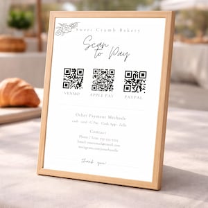 May include: A framed sign for Sweet Crumb Bakery with the text "Scan to Pay." It displays QR codes for Venmo, Apple Pay, and PayPal. Additional payment methods are listed below the QR codes. Contact information and a thank you message are also included.