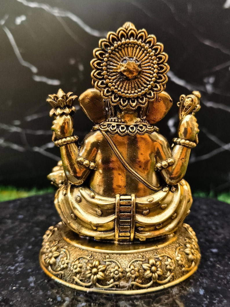 K&ouml;nnte beinhalten: Eine metallisch goldfarbene Figur einer Gottheit von hinten gesehen, mit einem gro&szlig;en kreisf&ouml;rmigen Heiligenschein, vier Armen mit erhobenen H&auml;nden, die Gegenst&auml;nde halten, und einer sitzenden Haltung auf einem runden Sockel mit floralen Schnitzereien.