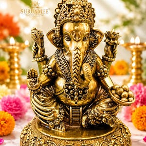 K&ouml;nnte beinhalten: Eine goldfarbene Statue der Gottheit Ganesha mit aufwendigen Schnitzereien, einer Krone und vier Armen. Die Figur sitzt auf einem runden Sockel mit Blumenmustern und h&auml;lt eine Schale mit S&uuml;&szlig;igkeiten in der einen und einen Gegenstand in der anderen Hand.