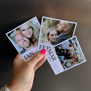 May include: A hand holding three small photo calendars. Each calendar features a different photograph and the months of January, February, and March 2026. The hand has bright pink nail polish and a white watch.