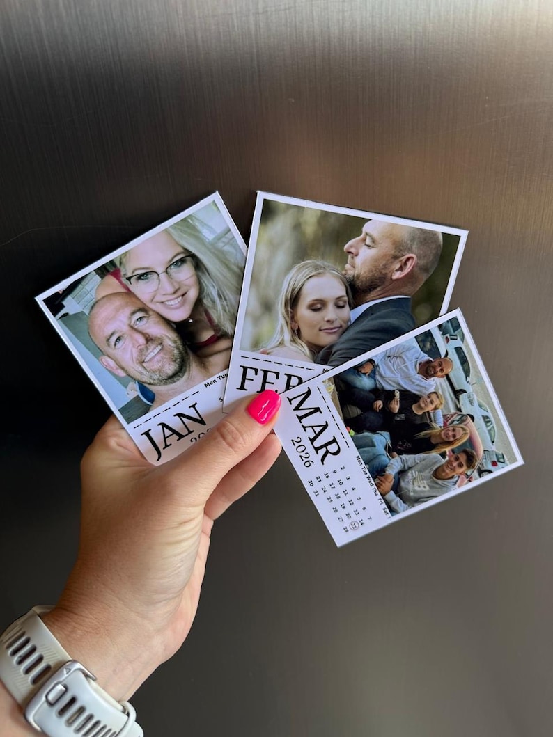 May include: A hand holding three small photo calendars. Each calendar features a different photograph and the months of January, February, and March 2026. The hand has bright pink nail polish and a white watch.