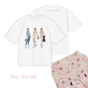 以下が含まれることがあります： さまざまな服装の女性3人のグラフィックが描かれた白いオーバーサイズのTシャツ。「I'm not mature enough for this」というテキストが背面にあります。ドレスやアクセサリーの模様が入ったピンク色の生地が見えます。