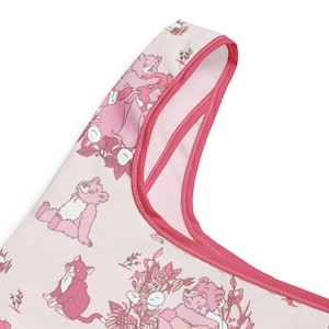 May include: A light pink tote bag with a repeating pattern of pink bears, cats, and floral elements. The bag has a contrasting dark pink trim and handles. The design is whimsical and playful, suitable for carrying groceries or personal items.