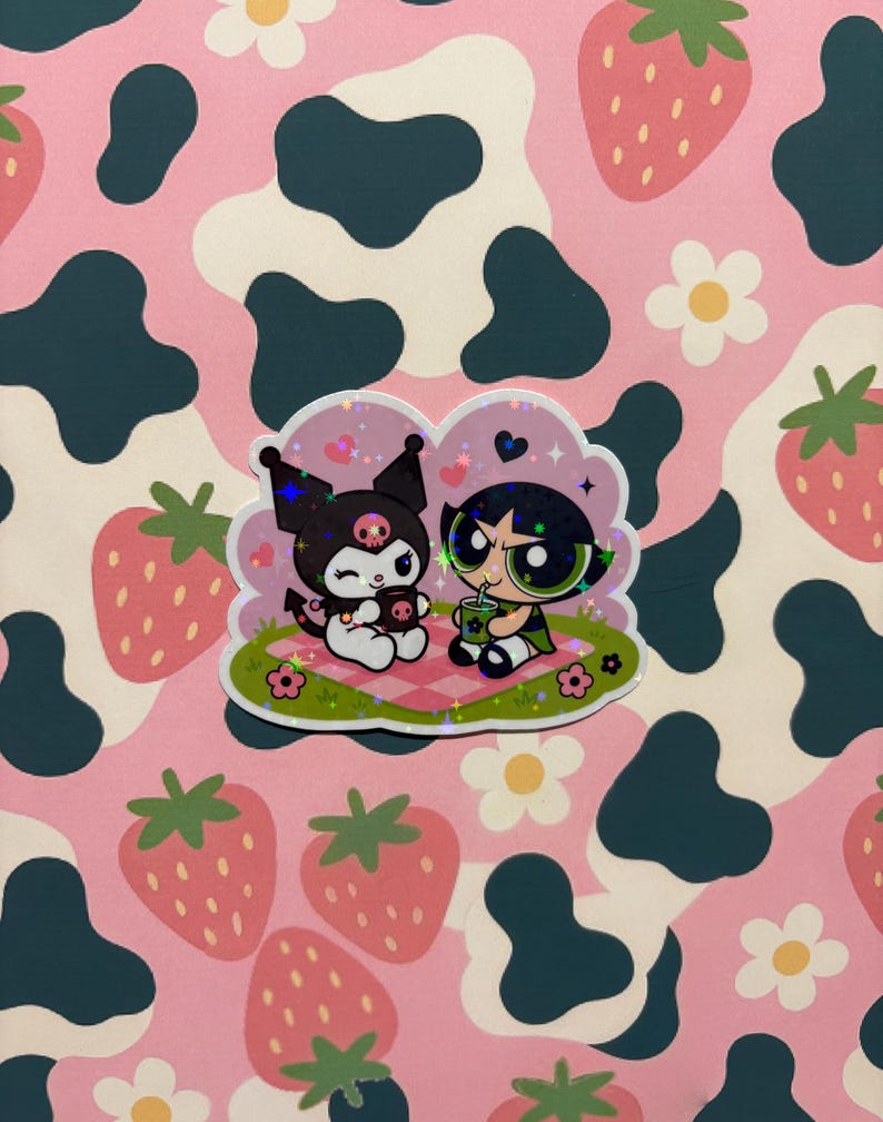 May include: A holographic sticker featuring the character Kuromi and Buttercup from The Powerpuff Girls sitting on a pink and white checkered picnic blanket. The design includes small hearts, flowers, and green grass with a sparkling star effect.