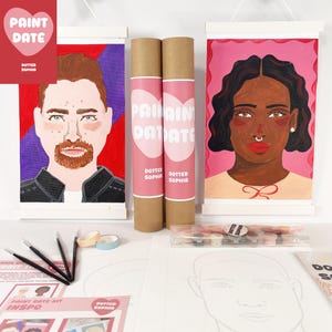 Op de afbeelding: Paint Date kits met portretten, penselen en kunstbenodigdheden. De kit bevat twee opgerolde doeken met de tekst "PAINT DATE" en "DOTTED SOPHIA". De portretten zijn van een man en een vrouw. De kit bevat ook penselen, tape en een palet.