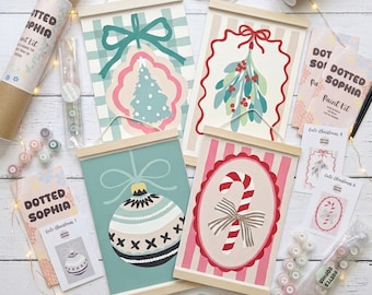 Puede incluir: Un kit de pintura Dotted Sophia que incluye cuatro láminas decorativas colgantes con motivos navideños como un árbol, muérdago, una bola y un bastón de caramelo, junto con botes de pintura, pinceles y tarjetas de instrucciones.