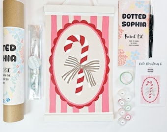 Puede incluir: Un kit de pintura por números Dotted Sophia con una ilustración de bastón de caramelo sobre un lienzo de rayas rosas y blancas con un marco ovalado festoneado. Incluye un tubo de cartón, botes de pintura, dos pinceles, guía y tarjeta.