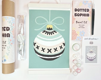Puede incluir: Un kit de pintura Dotted Sophia que incluye un lienzo colgante con un adorno navideño en color verde azulado, blanco y negro. El set contiene un tubo de cartón, un folleto de instrucciones, dos pinceles, una cinta adhesiva y botes de pintura numerados.