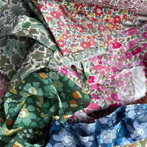May include: A collection of floral fabric swatches in various colors. The fabrics feature a variety of flower patterns in shades of red, pink, blue, green, and purple. The image showcases the textures and colors of the fabric.